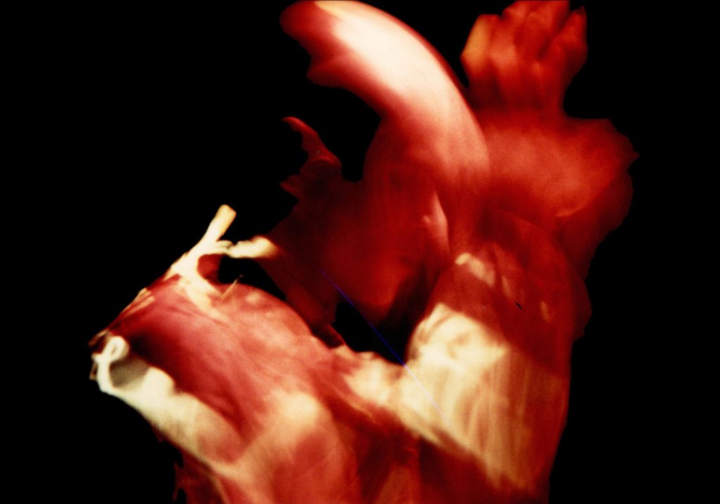 This image features James Keane conducting music. He faces to the right, is lit in red, and the image is blurred for artistic effect.