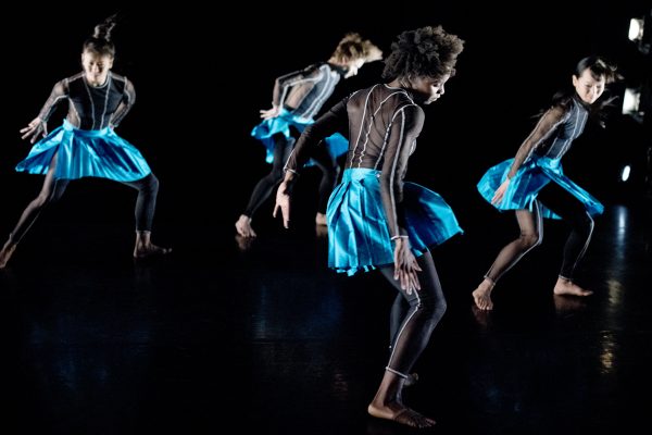 Four dancers are dressed identically in blue skirts dancing.