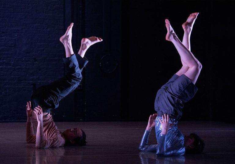 Two dancers resting on their shoulders with their torsos and legs in the air.